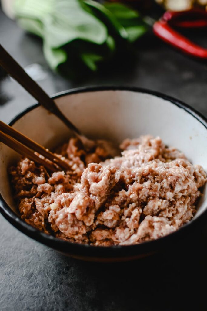 Raw ground pork in a bowl with chopsticks, ready for culinary preparation.